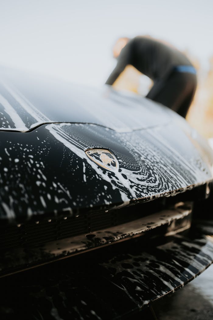 Close-up of a luxury sports car under soap suds during a detailed wash.