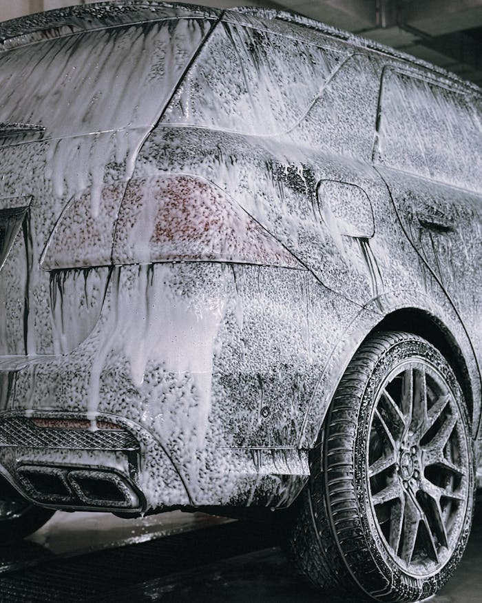 A premium SUV being cleaned with foamy soap in a detail car wash facility.